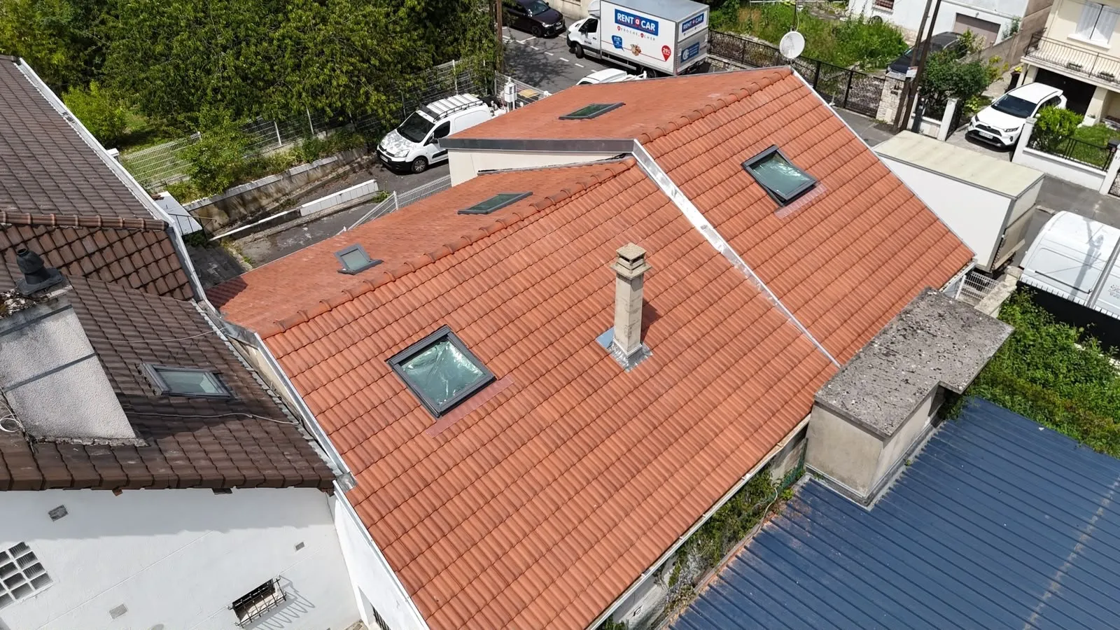 Vue d’ensemble d’une toiture en tuiles orangées avec des fenêtres de toit et une cheminée.