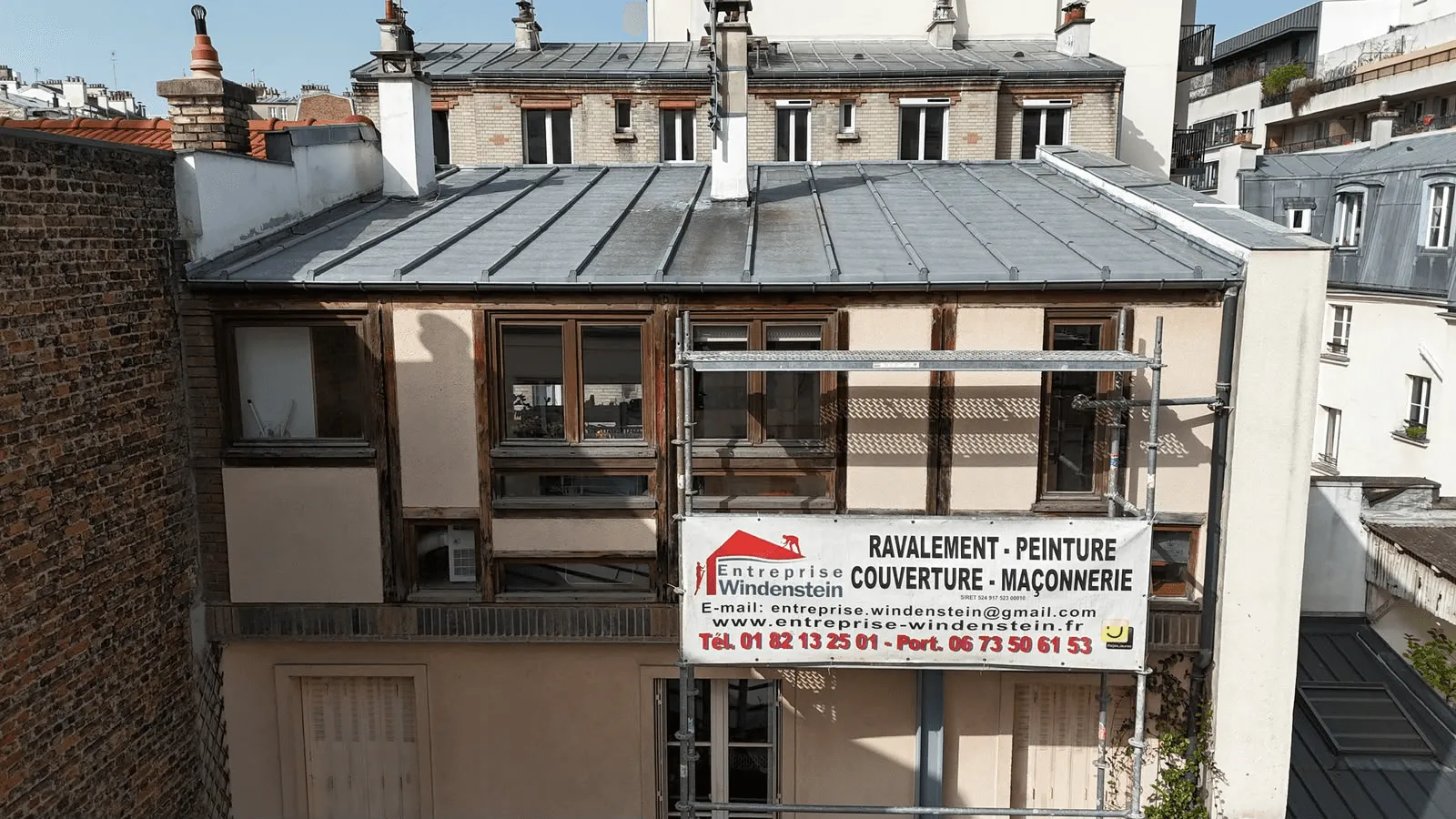 Toiture grise avec une gouttière visible sur le bord droit, une fenêtre de toit et plusieurs cheminées